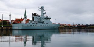 Ein Militärschiff liegt im ruhigen Hafen. Der Himmel ist weiß-grau