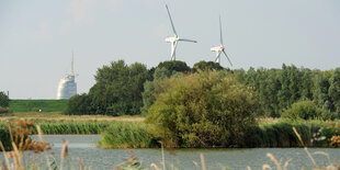 Ein Gewässer, im Hintergrund zwei Windräder