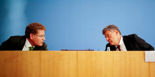 Patrick Graichen und Robert Habeck lehnen sich mit ernsten Gesichtern zueinander hin.