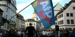 Eine AfD Fahne weht im Vordergrund, Höcke spricht auf dem vollen Marktplatz von Döbeln, er ist von hinten zu sehen