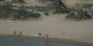 Eine Frau spielt mit einem Ball vor einem verbrannten Wald an einem Strand auf Rhodos