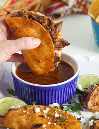 Birria Taco being dipped in a blue bowl of Birria stew.