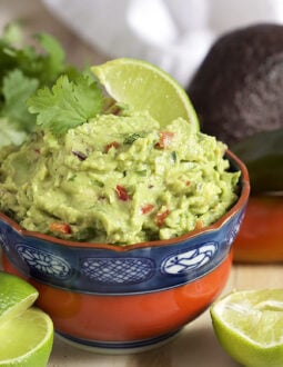 Guacamole in a red and blue bowl with a lime in it.