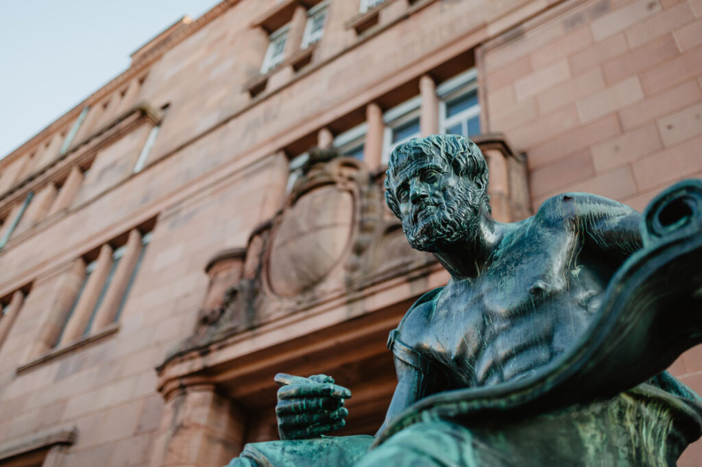 Eingang zum Kollegiengebäude 3 der Universität Freiburg mit der davorstehenden Aristoteles Statue.