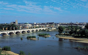 Photo en couleurs d'un large fleuve traversé par un pont ; une ville en arrière-plan.