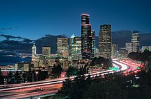 Skyline of city at dusk. A major highway winds itself into the downtown area.