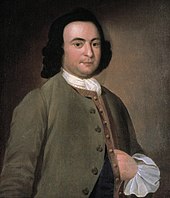 Der junge George Mason steht vor hellem Hintergrund mit einem rotem Anzug.