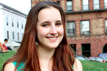 Headshot of Emily Temple-Wood standing outside. She is a young white woman with red hair wearing a green dress.