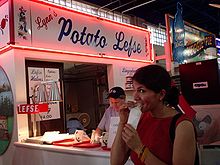 chest high portrait of a woman customer eating in front of neon-lit Lynn's Potato Lefse stand