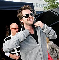 A picture of a man with dark hair wearing sunglasses and a grey top