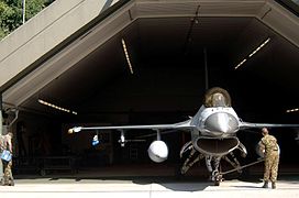 Un caça F-16 davant d'un hangar protegit.