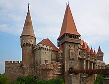 Photographie en couleurs d'un château aux remparts crénelés et aux nombreux donjons, relié à la terre par un seul pont.