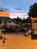 People on a street in the sunset under some gazebos and a person walking a dog