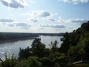 A wide river flows atween dark forests an law bluffs