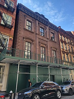 A three story brick building whose lowest floor is covered by a green sidewalk shed.