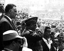 Several men in different clothing standing before a crowd of people.