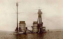 The top of a warship juts out of calm water after it had been sunk