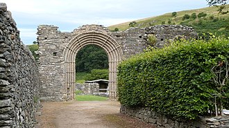 Ruins of stone walls and an ornate walkway in a valley with greenery all around