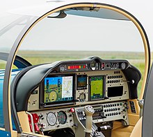 The image shows the cockpit of a DR401-155CDI, the old style instrument is replaced by a full glass cockpit. No old gauges can be seen. The stick has also been reworked to offer a trim directly on it, as well as an Autopilot disconnect button.