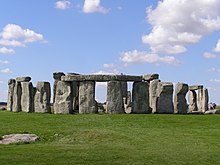 Sun shining through row of upright standing stones with other stones horizontally on the top.