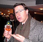 Photographie d'un homme avec des lunettes portant une peluche dans la main.