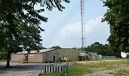 A one-story gray metal building with a W L I W logo next to the base of a tall broadcasting tower