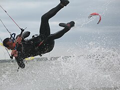 Kitesurfer wearing one-piece wetsuit, hanging from harness, separated from board.