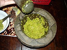 a grey, stone mortar is shown from above, containing a bright green, slightly lumpy paste