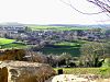 Roofs of houses visible amongst green fields and hedgerows. Large rock in the foreground.