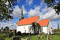 Foto einer weißen Kirche mit rotem Dach. Im Vordergrund ein Friedhof.