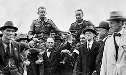 Deux hommes en uniforme portés et entourés par une foule de personnes.