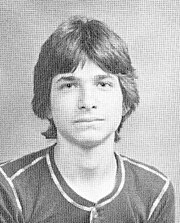 Black-and-white headshot of a young man with medium-length middle-parted hair, wearing a collarless button-up shirt