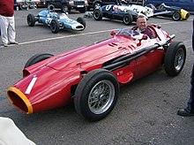 Photo de profil gauche d'une Maserati 250F rouge en exposition, avec un visiteur à son bord