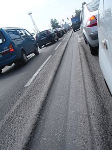 A fragment of a road surface, heavily rutted by car wheels following the same path.