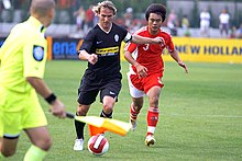 Două players vying for the ball, with a linesman nearby