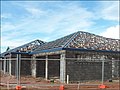 A hip roof construction in Northern Australia showing multinail truss construction. The blue pieces are roll formed metal roof battens or purlins. This roof is built with purpose-made steel hook bracket which is bolted to the truss with M16 bolt. The bracket is bolted to an M16 bolt cast in situ, embedded 300 mm (12 in) into the reinforced concrete block wall. This system is typically in place every 900 mm (35 in) around perimeter