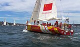 yellow, red and white boat in the middle of the blue sea with a red flag and people on it.