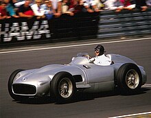 Photo couleur de Fangio, pilotant une Mercedes-Benz W196 grise en 1986