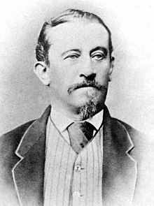 Portrait photo of Fran Levstik posing in a suit and tie. His dark-colored suit has a light-colored edge on the lapel, and his buttoned-up vest is lightly pinstriped.