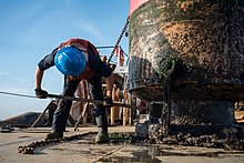 A sailor scrapes barnacles and other marine growth off of a buoy