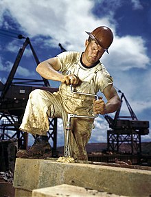 Carpenter in a hard hat using a hand drill outdoors