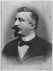 Léon Tailhade avec bouc et moustache, vêtu d'une veste, avec un nœud papillon sur une chemise à col droit.