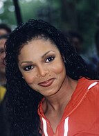 Janet Jackson smiling for the camera in an orange jacket.