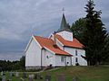 Foto einer weißen Holzkirche, im Vordergrund ein Friedhof