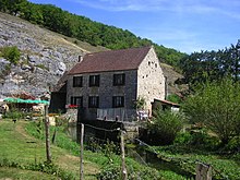 Photo d'une grande maison rectangulaire appuyée contre la falaise.