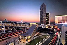 A train station built over a busy intersection in front of several skyscrapers at sunset.