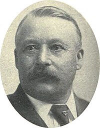 Portrait photograph of a man with a mustache in a suit and tie