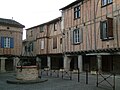 photo couleur de maisons sur une place à couverts. Le rez de chaussée comporte des portiques. Les étages sont à colombage garnis de brique foraine.