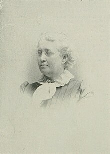 B&W portrait photo of a white-haired woman wearing a white, flouncy blouse, and buttoned jacket.