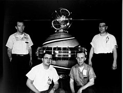 Four men pose by a spherical satellite